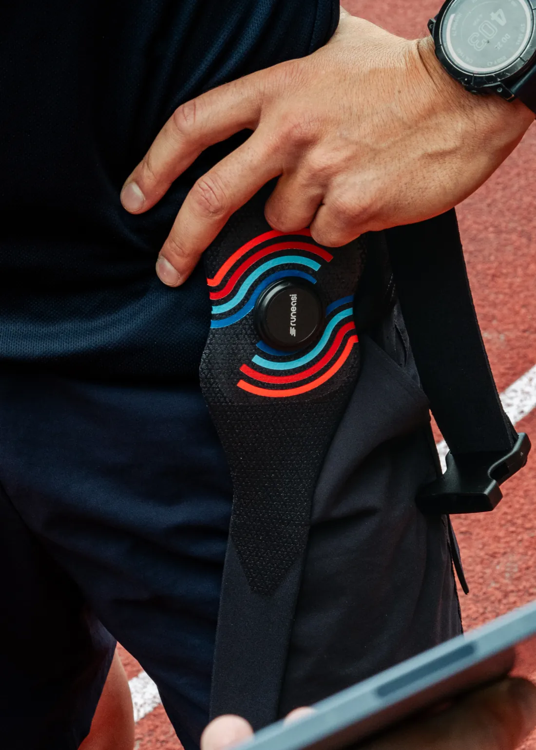 A hand rests on a runner's hip beside the Runeasi belt and sensor