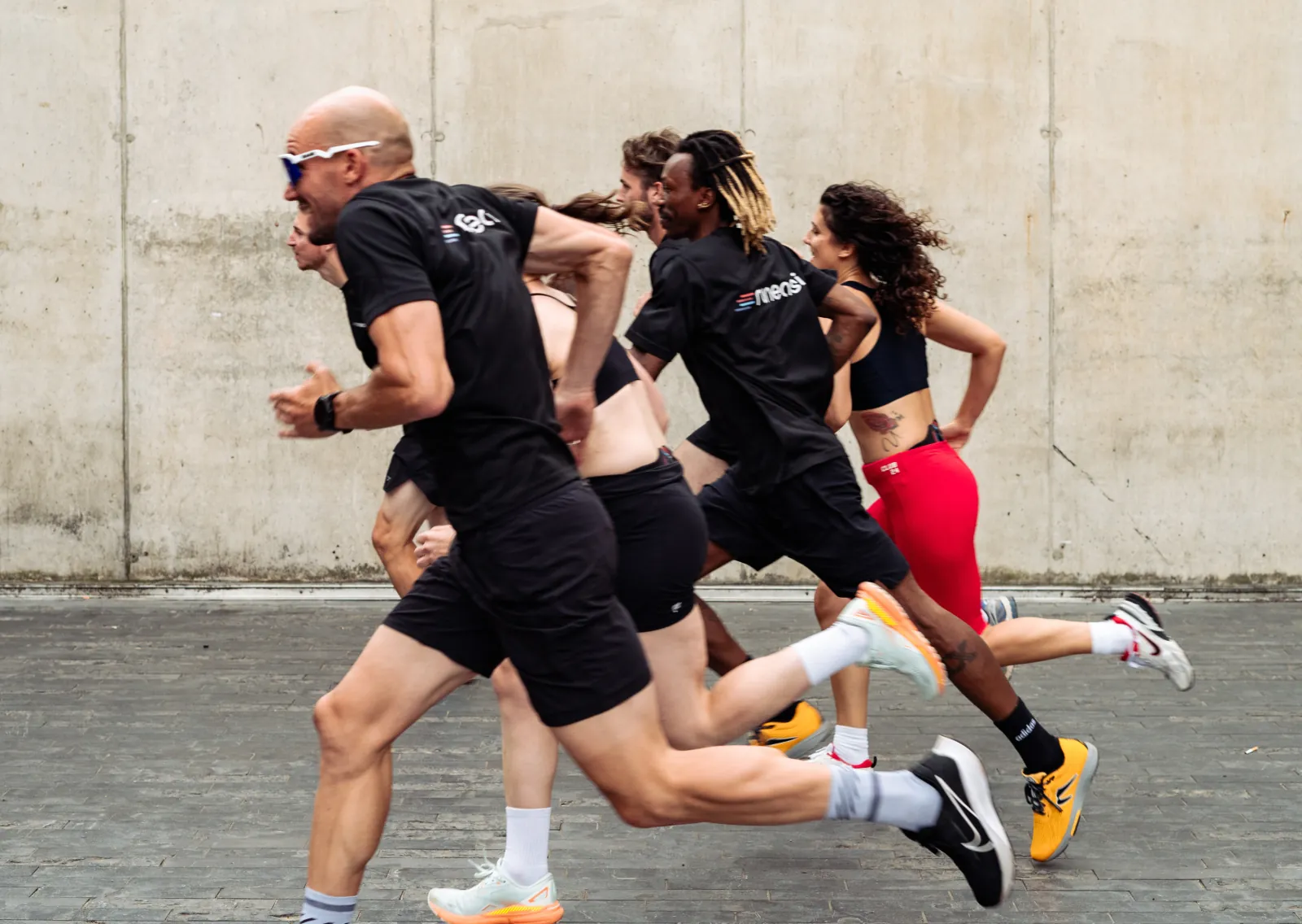 Four runners sprinting past a concrete wall