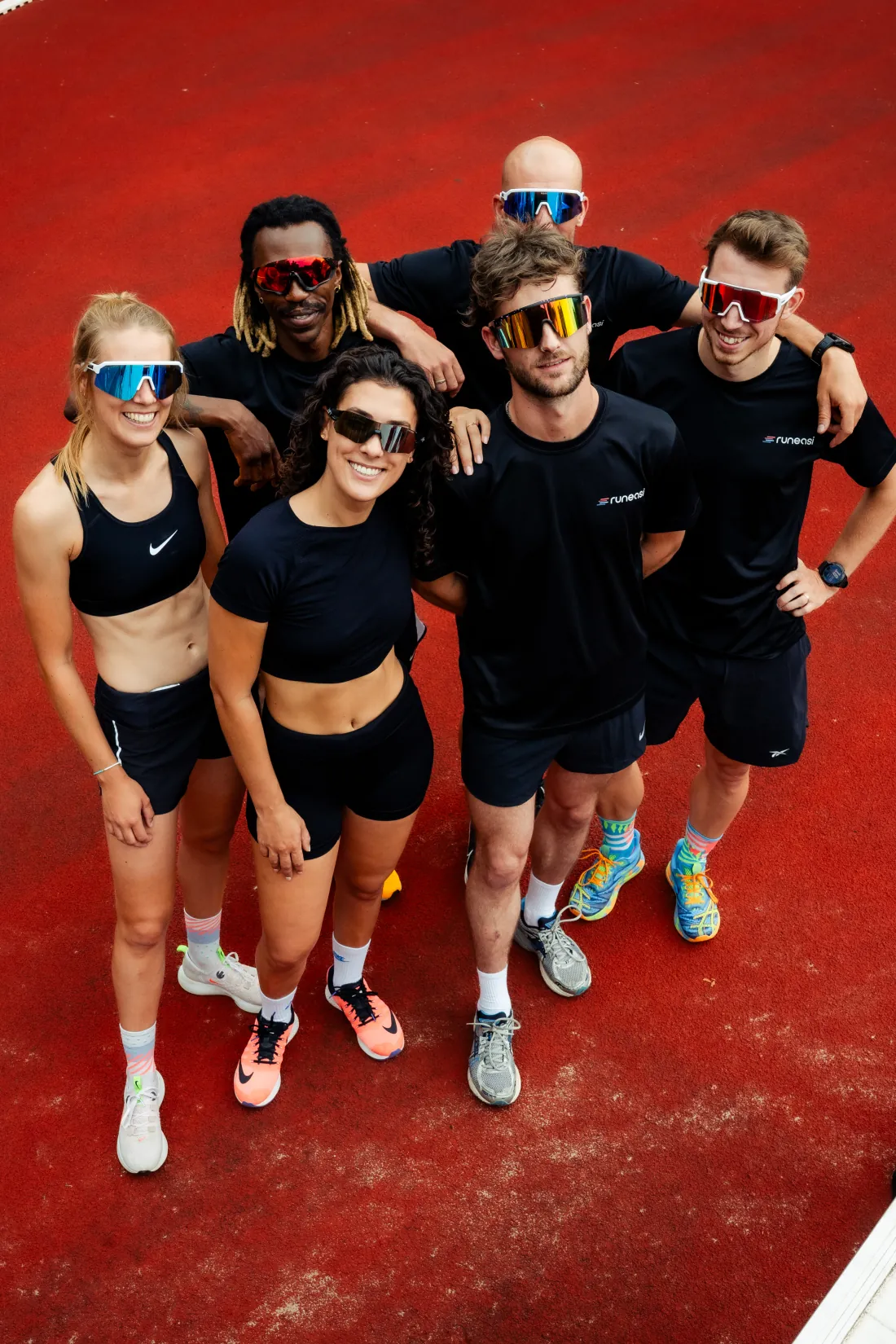 Six runners smiling at the camera on a red running track