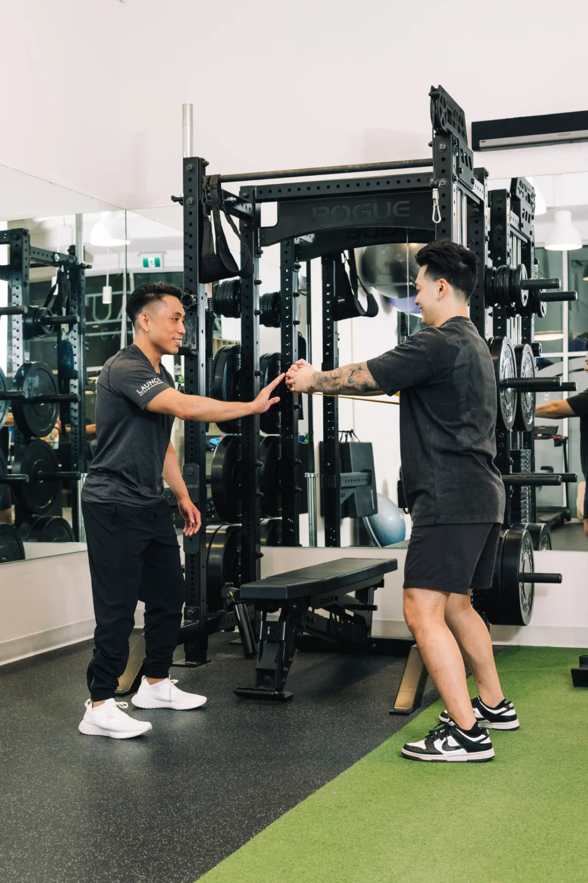 A Launch Rehab physiotherapist guiding a client through a resistance band exercise beside a squat rack