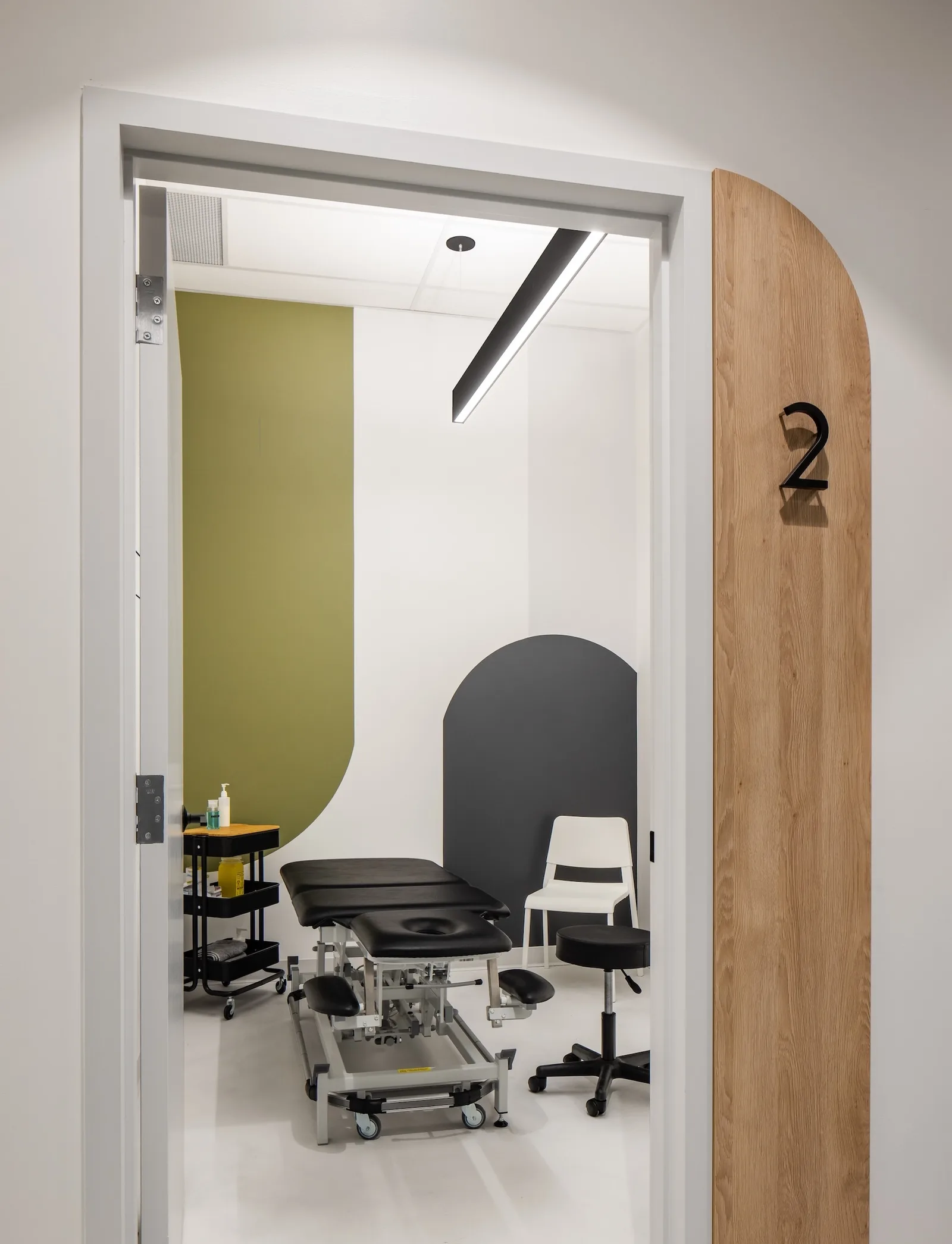 Treatment room at Launch Rehab New Westminster viewed through an arched wooden door numbered 2, with olive green and grey wall accents