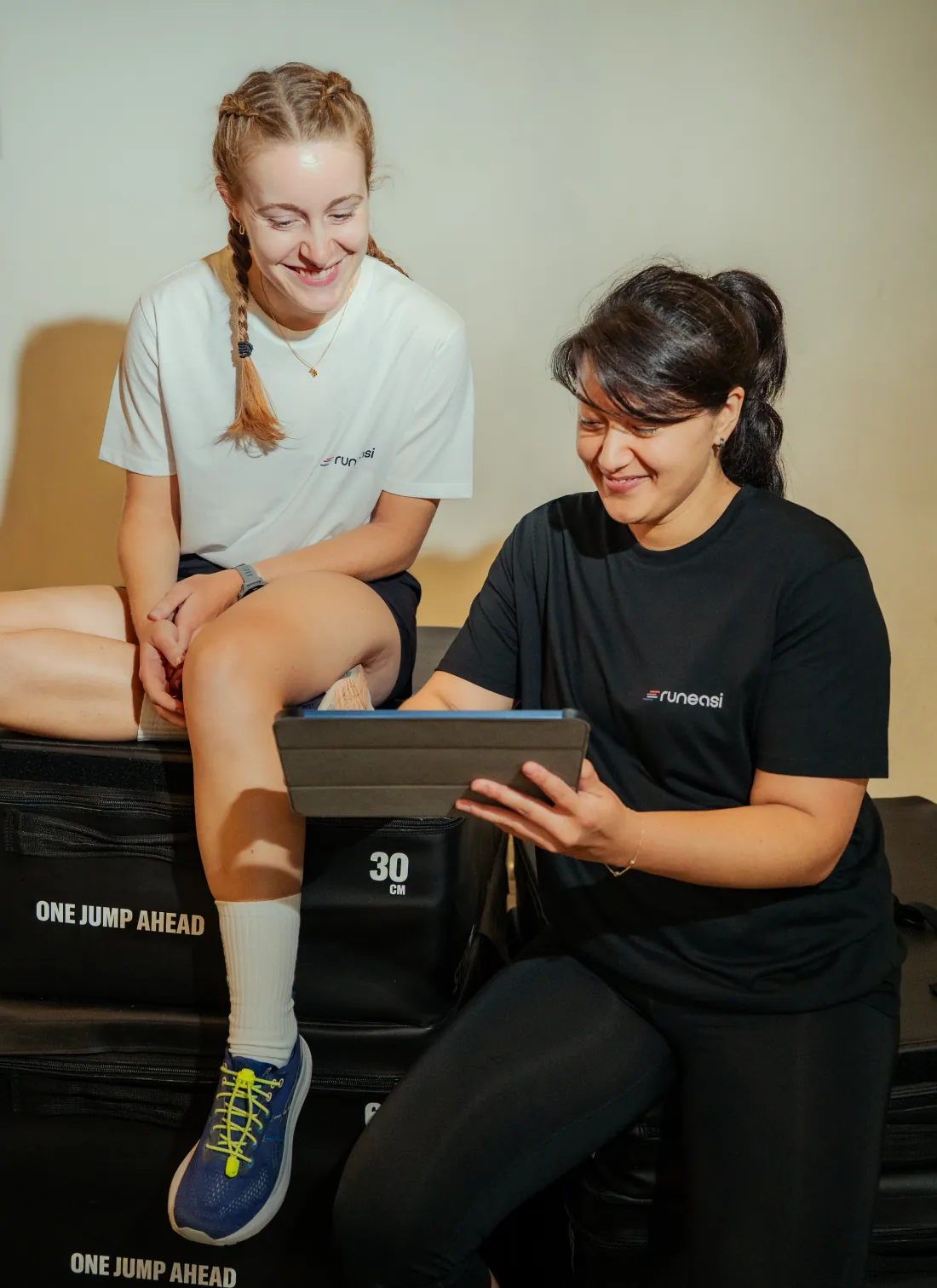 A runner sits on a jump box while a tester shows her the results on a tablet