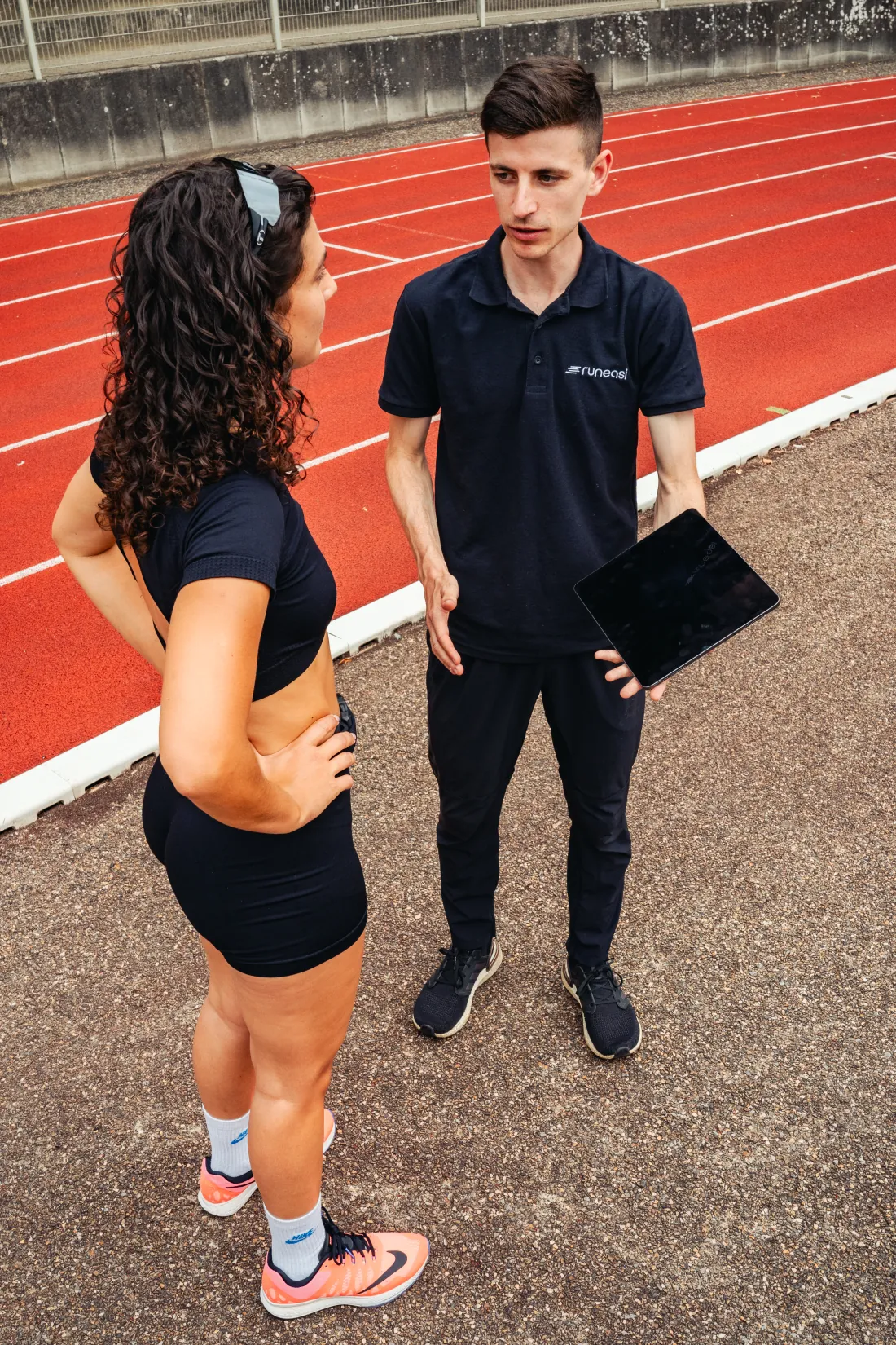 A tester holding a tablet talks with a runner on a running track