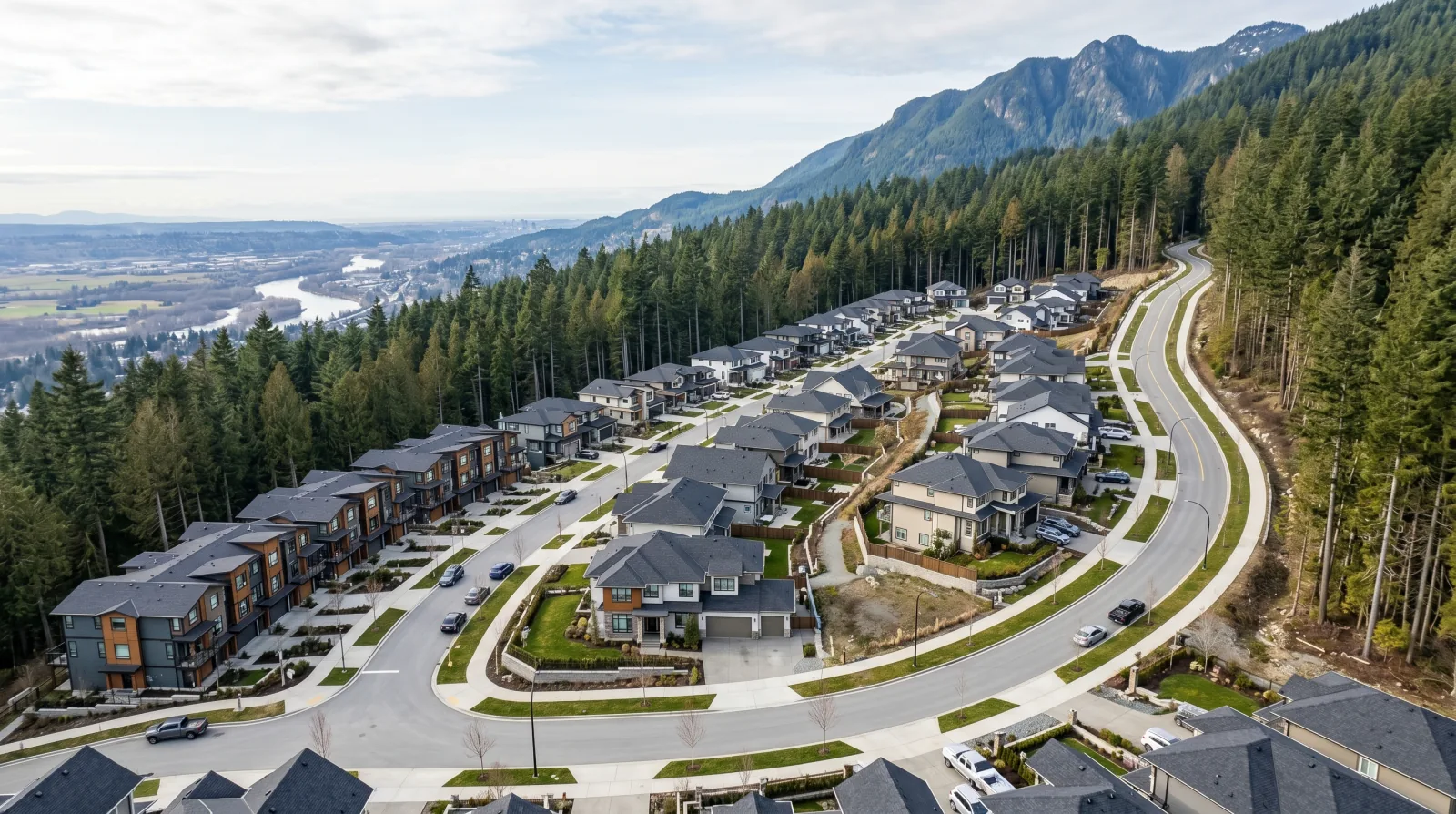 A new master-planned subdivision of houses and townhomes climbing a forested mountainside with a river valley below — evoking the Burke Mountain neighbourhood in northeast Coquitlam.