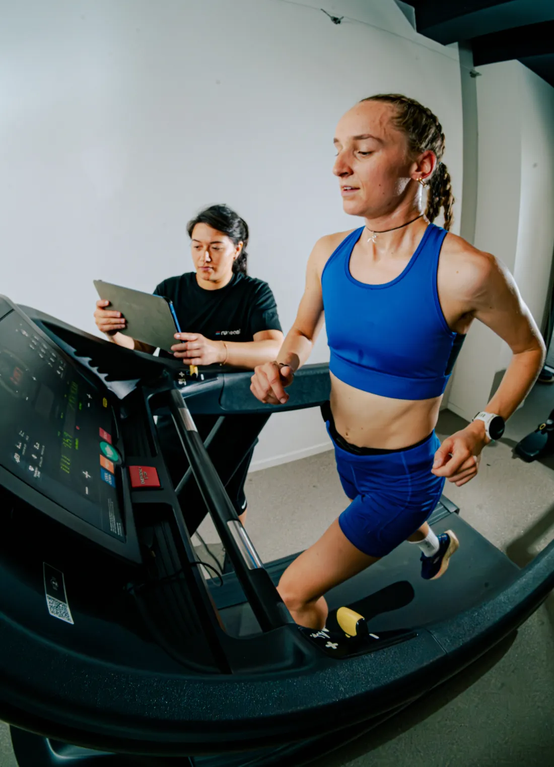 A runner on a treadmill while a tester beside it follows the data on a tablet