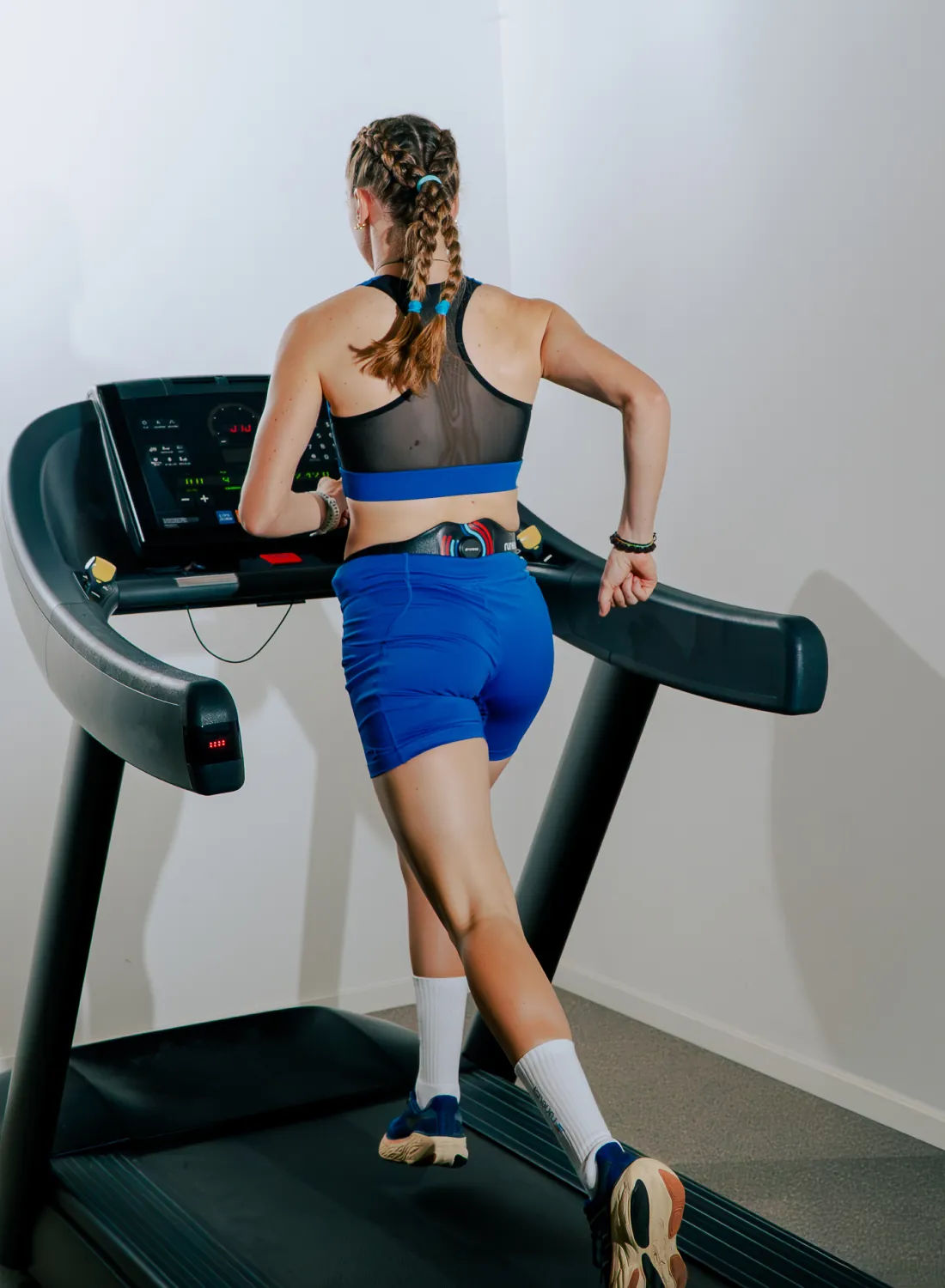 A runner on a treadmill seen from behind, with the Runeasi sensor on her lower back