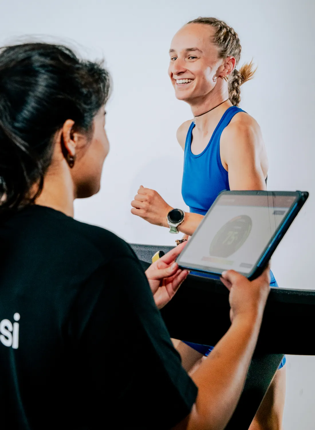 A tester with a tablet talks with a smiling runner on a treadmill