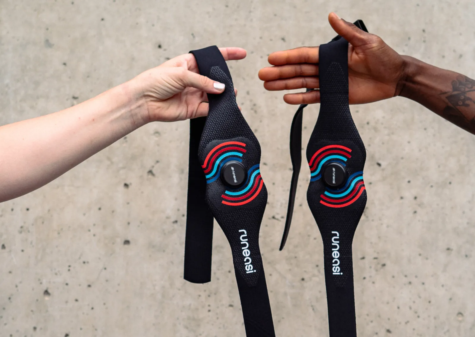 Two hands each holding a Runeasi belt in front of a concrete wall